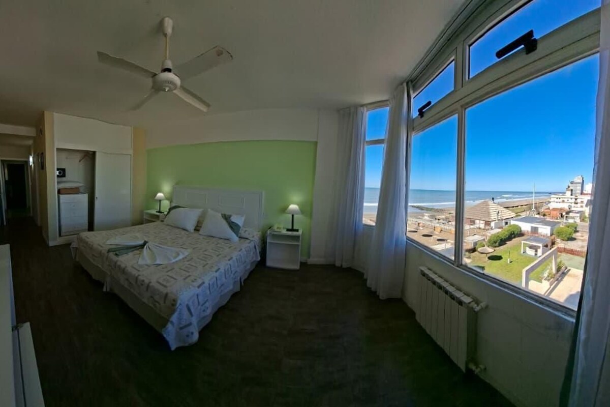 Una camera da letto con un letto, comodini, una ventola a soffitto e vista sulla spiaggia.