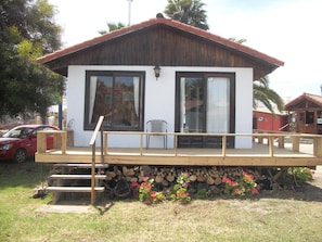 A small, single-story building with a wooden deck, large windows, and a stone foundation. - Cabañas MarSerena (La Serena)