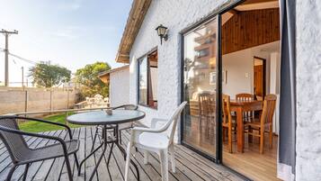 An outdoor patio with a round table and chairs, wooden deck, and a view of the interior through a glass door.