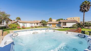Un jacuzzi rodeado por una piscina, con un cielo azul despejado.