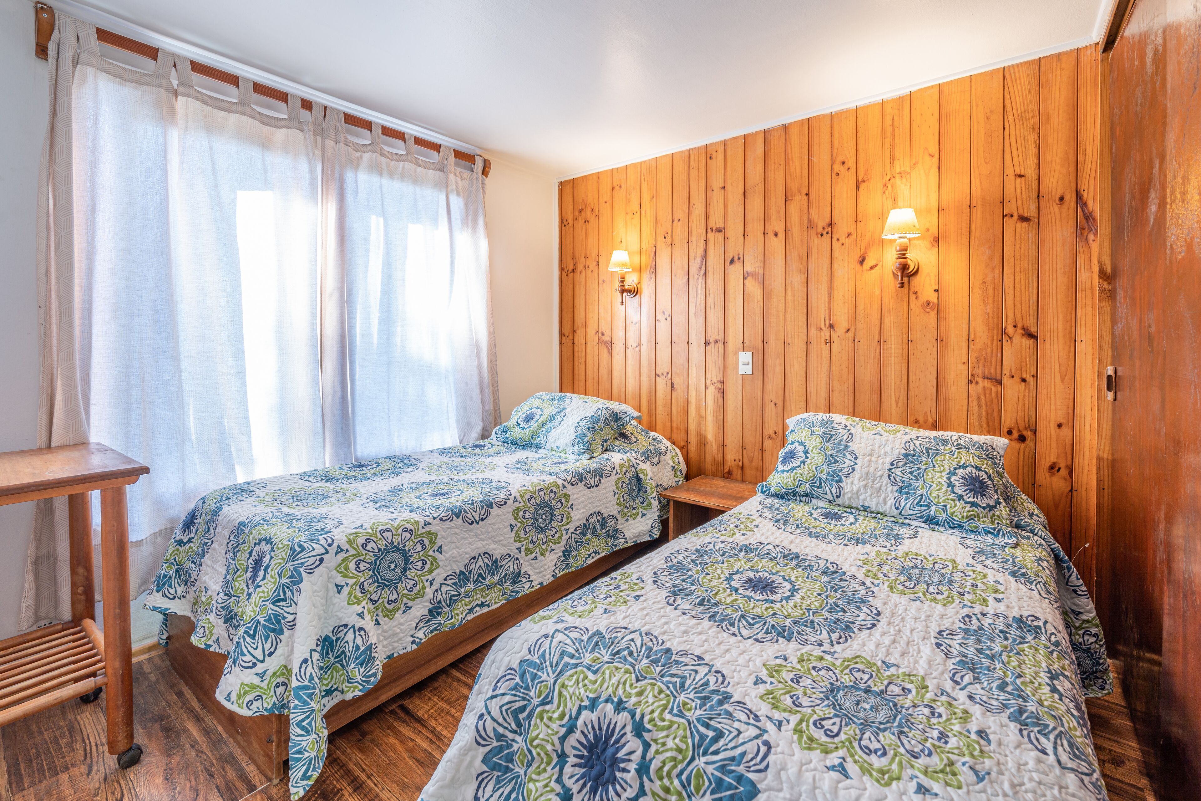 Una habitación con dos camas, paredes de madera y una ventana con cortinas.