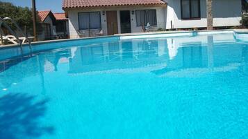 A clear blue swimming pool with a tiled deck, surrounded by buildings with red-tiled roofs and white walls.