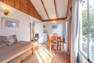 Una habitación acogedora con techo de madera, un sofá, una mesa de comedor con sillas y vistas a través de un ventanal grande.