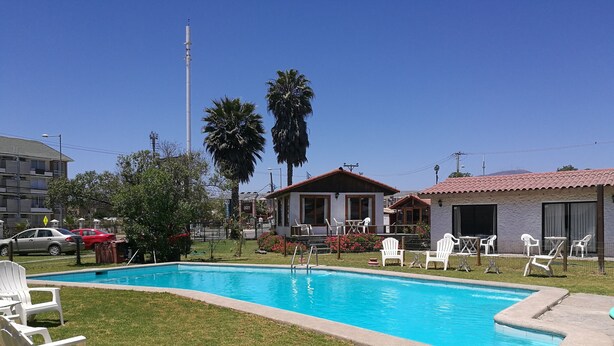 Ein Swimmingpool mit weißen Liegestühlen, umgeben von Rasenflächen und Palmen.