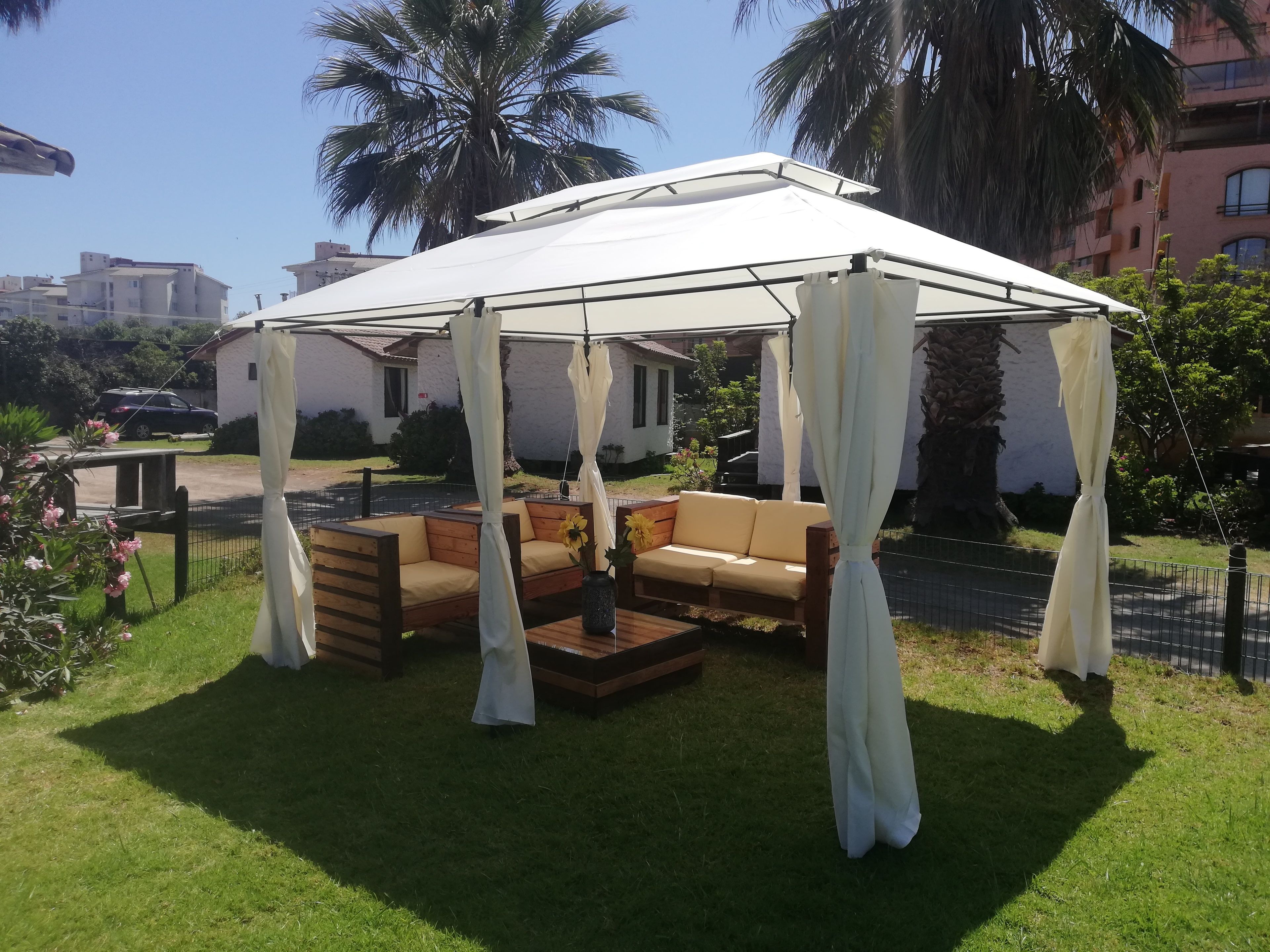 A covered outdoor seating area with a wooden bench and a sofa, surrounded by a white canopy.