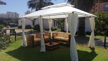 A covered outdoor seating area with a wooden bench and a sofa, surrounded by a white canopy.