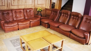 Ein braunes, ledernes Ecksofa, ein Holztisch und eine Vase mit gelben Blumen.