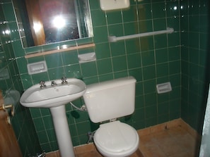 Une salle de bain avec des murs recouverts de carreaux verts, un lavabo blanc et des toilettes.