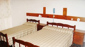 Une chambre avec deux lits simples, des têtes de lit en bois, une petite table de chevet et un téléphone fixé au mur.
