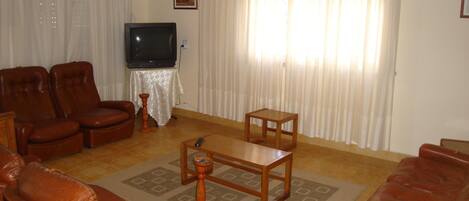 A living room with a sofa, chairs, a coffee table, a television, and curtains.
