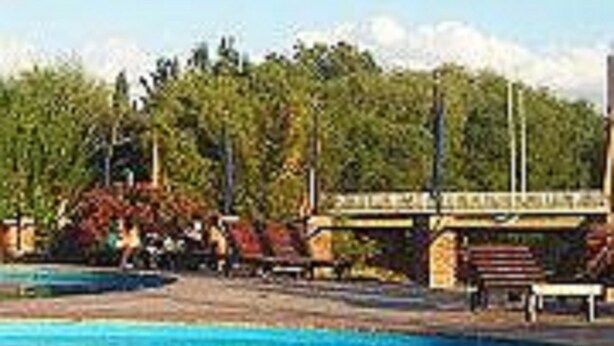 A swimming pool with a clear blue water surface, surrounded by trees and a bridge in the background. - Hotel Ruta 66 (Mina Clavero)