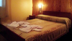 A hotel room with a wooden headboard, a bed with a patterned bedspread, and a nightstand with a lamp. - Hotel Ruta 66 (Mina Clavero)
