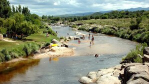 A river with people swimming and standing on the banks, surrounded by greenery and rocks. - Hotel Ruta 66 (Mina Clavero)