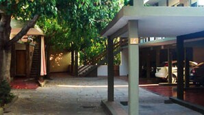 A covered outdoor area with a staircase leading to a building entrance, a parked car, and a tree providing shade. - Hotel Ruta 66 (Mina Clavero)