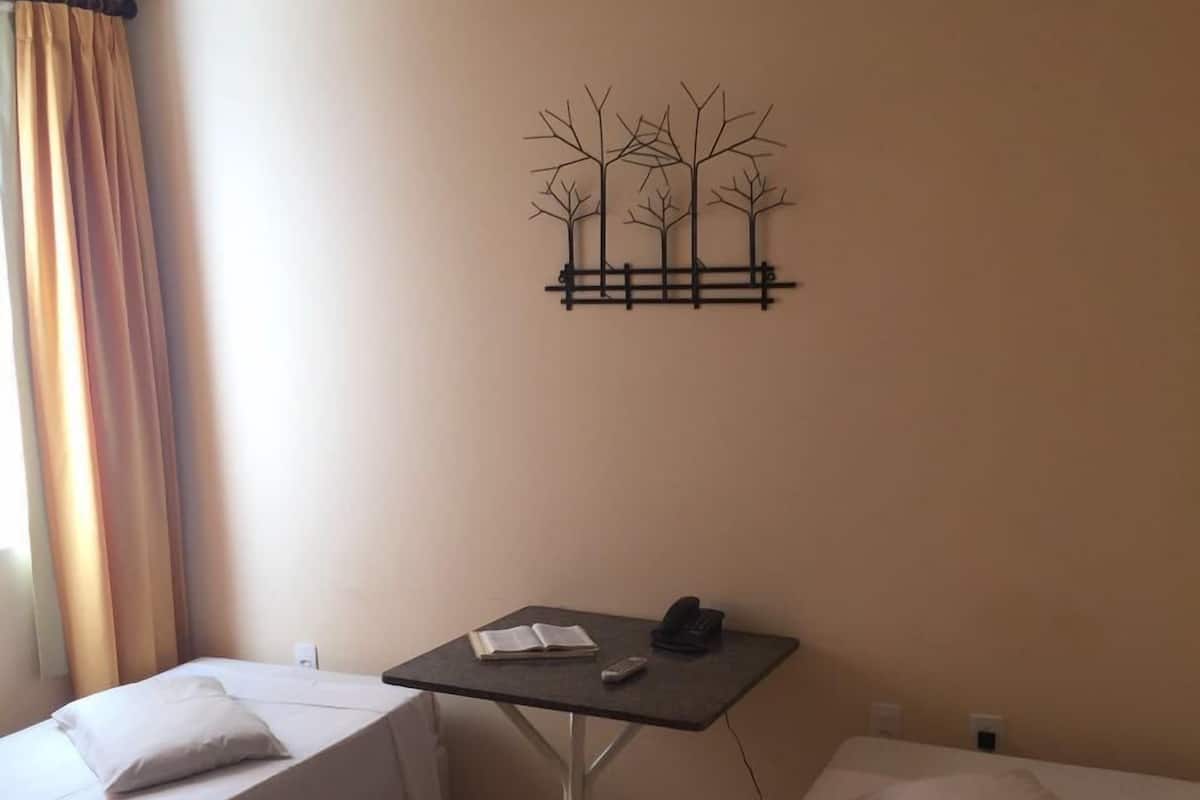 A hotel room with two beds, a small table with a book and a phone, and a wall art piece.