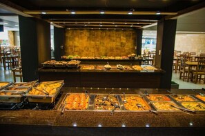 A buffet with various food options in a well-lit dining area with tables and chairs. - Hotel Trilhos de Minas (São João del Rei)