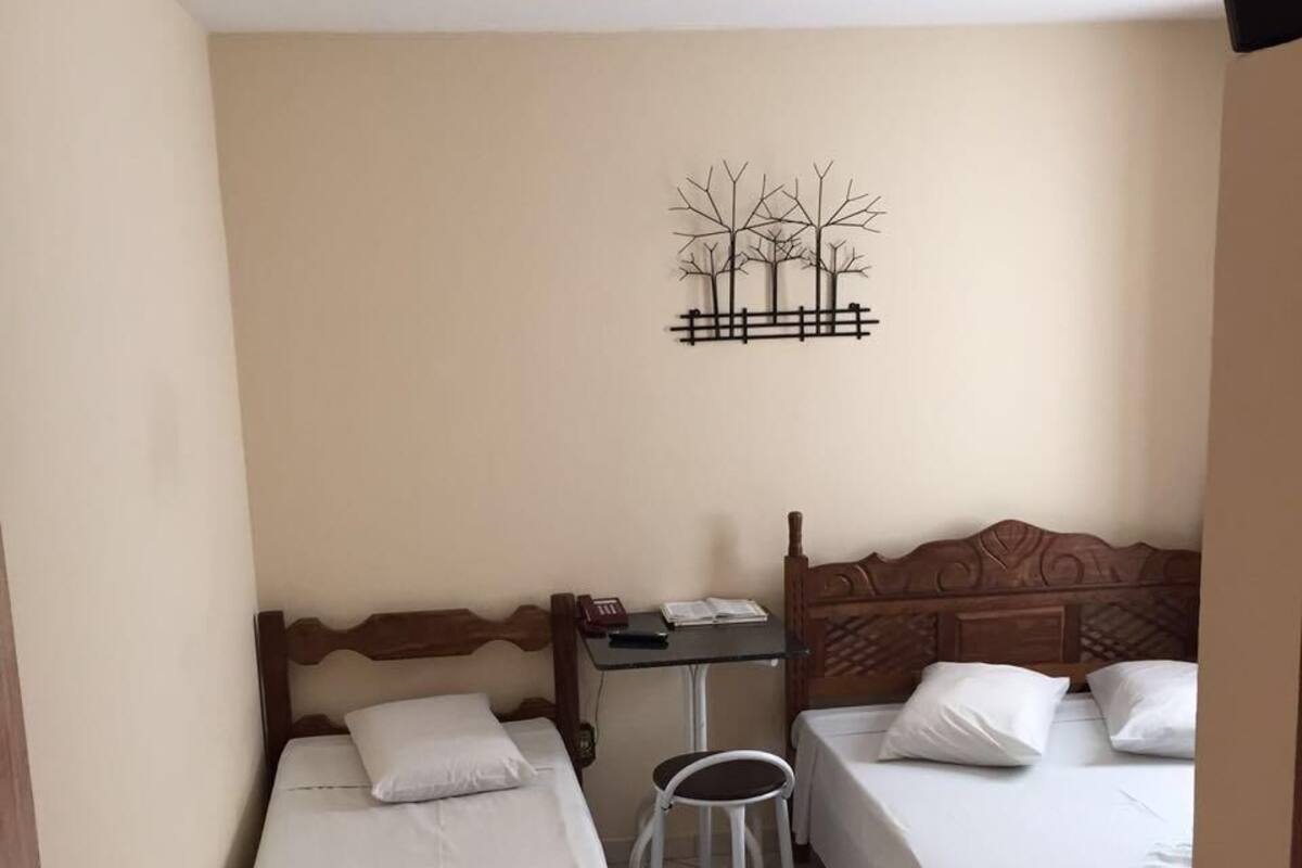 A small, clean room with two single beds, a small table with a chair, and a wall decoration.