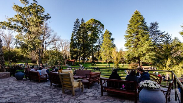 An outdoor seating area with stone flooring, wooden furniture, and a large flower pot. - Hotel Luz y Fuerza Villa Giardino (Villa Giardino)