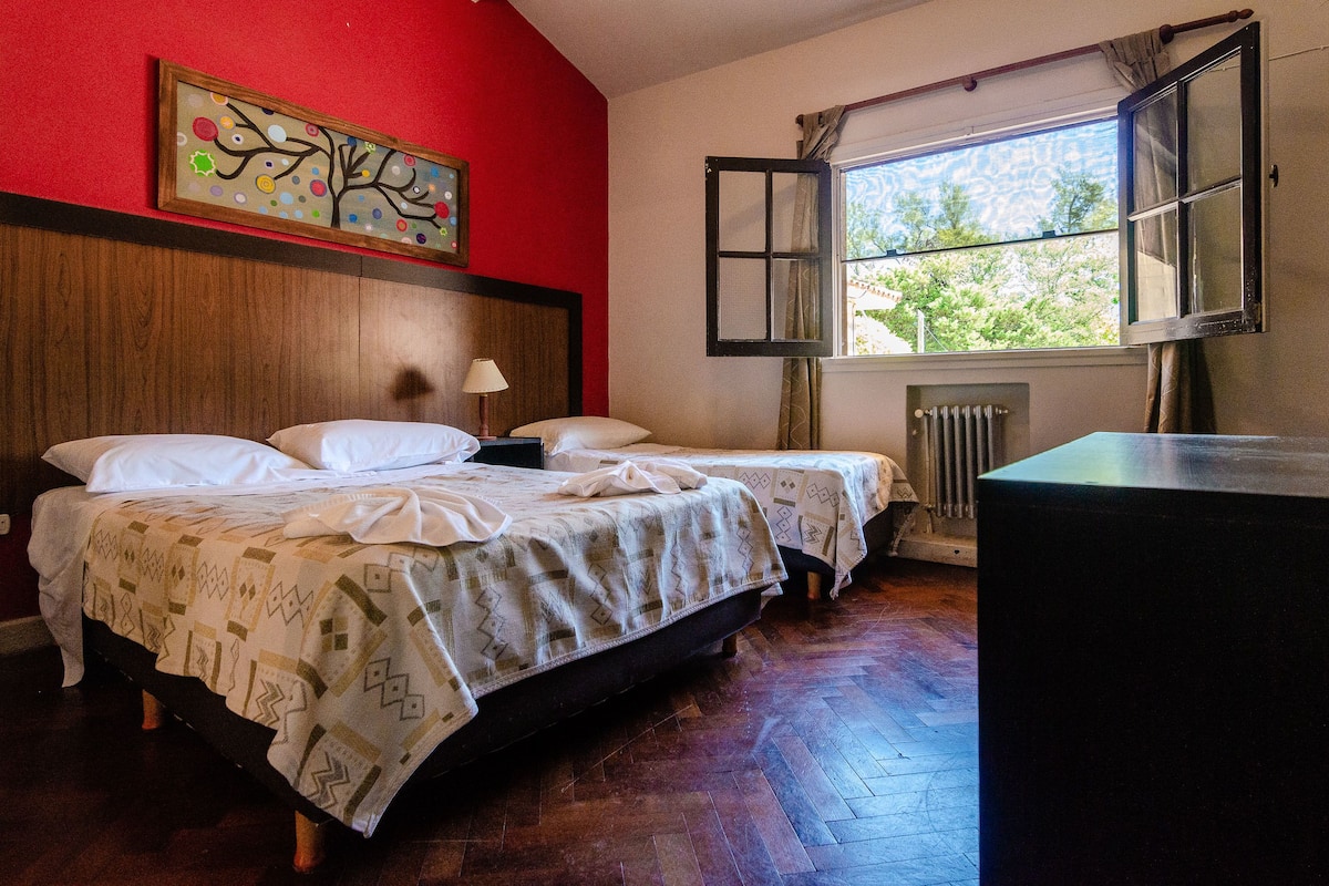 A room with two beds, a wooden headboard, a window with curtains, and a radiator.
