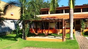 A courtyard with a hammock, palm trees, and a building with a tiled roof. - Pousada Vale da Montanha (Serra Negra)