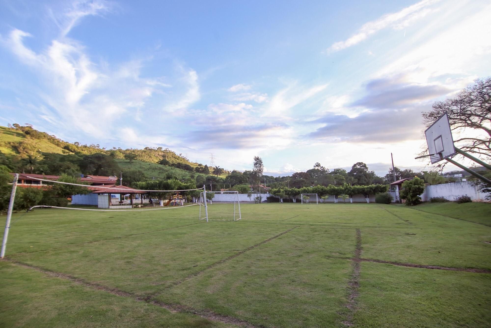 Um campo esportivo com uma rede de vôlei, postes de gol e uma cesta de basquete.