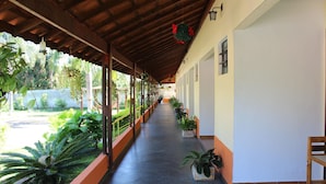 A covered corridor with a tiled floor, potted plants, and a wooden chair. - Pousada Vale da Montanha (Serra Negra)