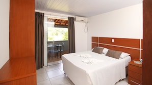 A hotel room with a bed, wooden headboard, a desk, and a sliding glass door leading to an outdoor area. - Pousada Vale da Montanha (Serra Negra)