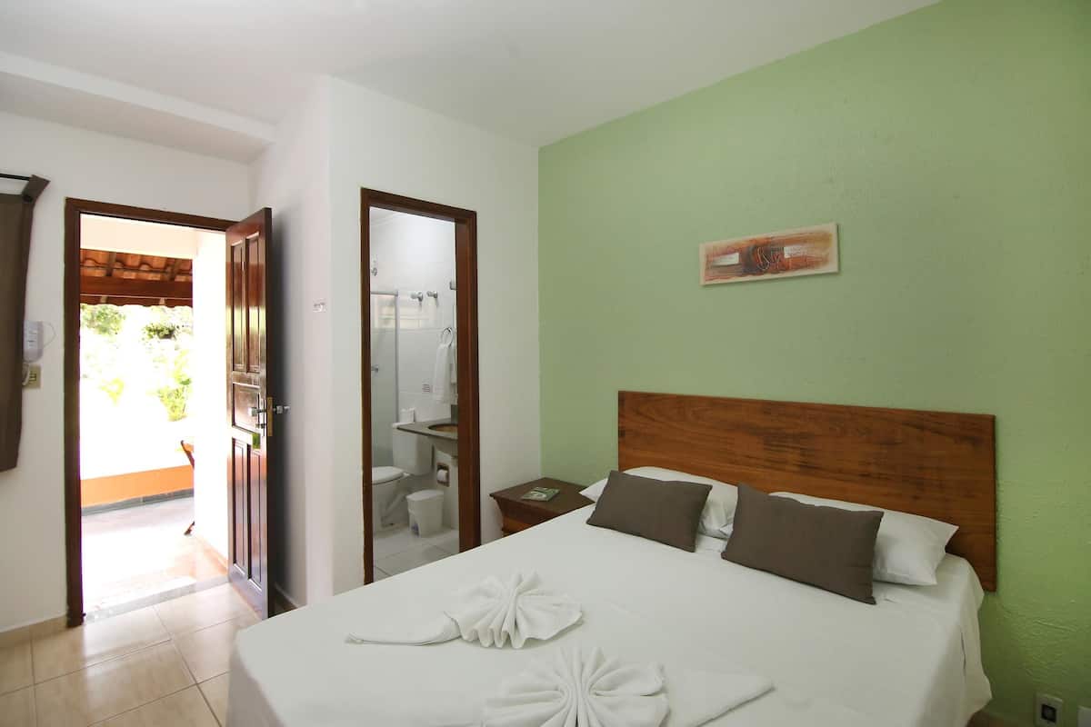 Quarto de hotel com uma cama, mesa de cabeceira, espelho e porta para o banheiro.