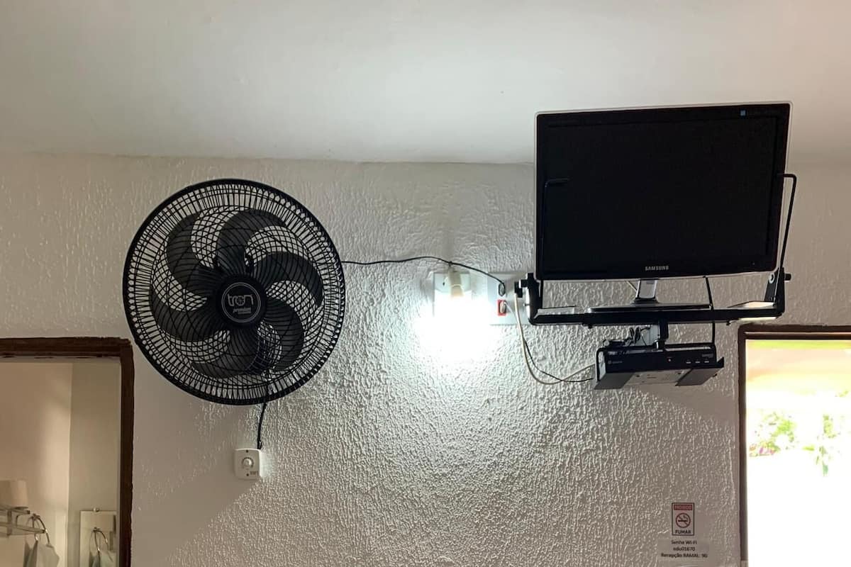 Quarto com ventilador de teto, televisão montada e porta com vista para o exterior.