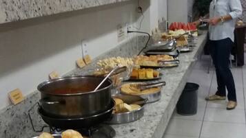 Disposição de buffet com diversos alimentos e uma pessoa servindo.