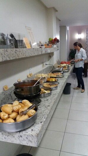 A buffet setup with various food items and a person serving.