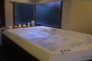 A large, rectangular hot tub with multiple jets, surrounded by candles, in a dimly lit room with large windows. - La Mansión del Bosque (Mar de Las Pampas)