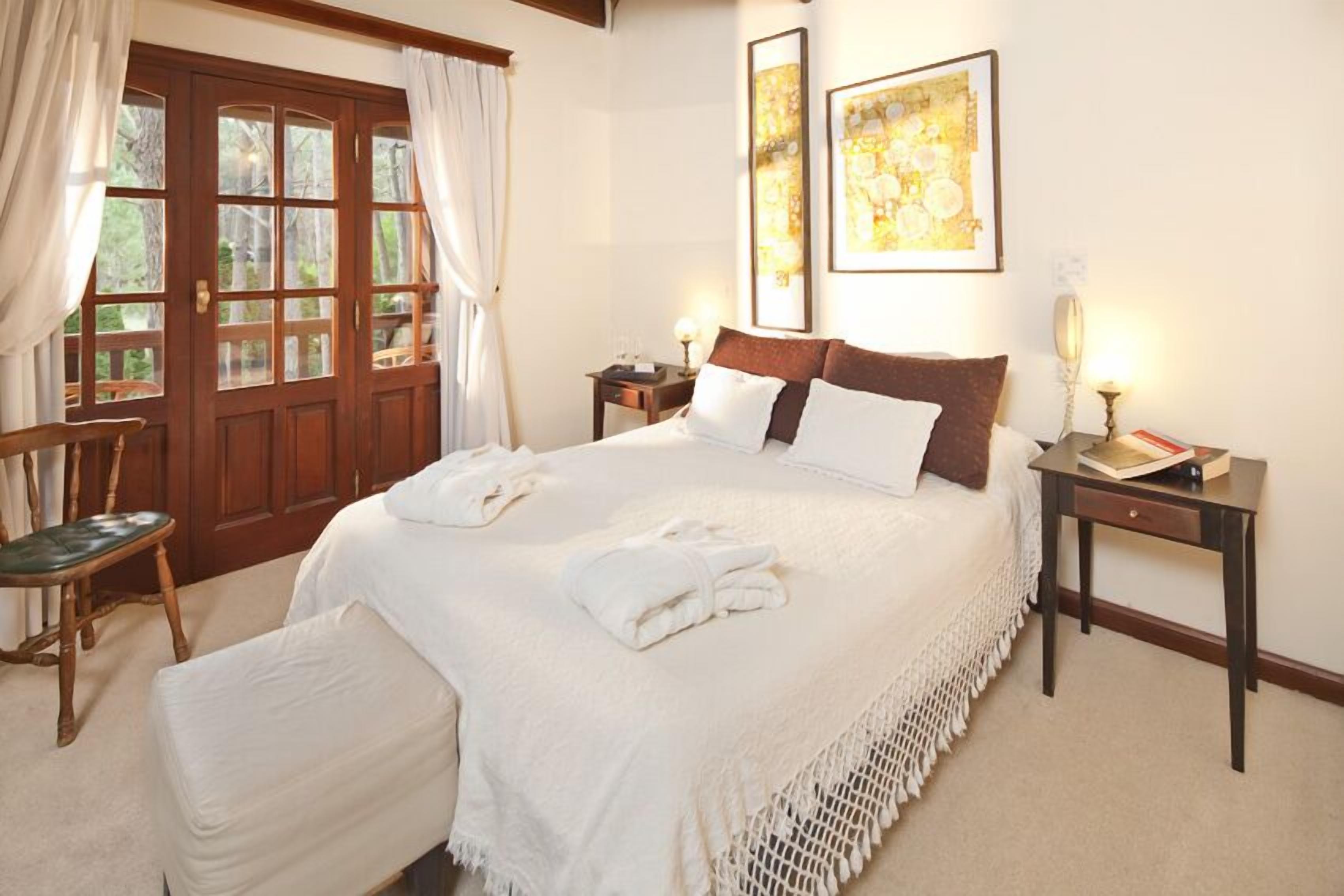 Un dormitorio ordenado con una cama grande, una silla de madera, una mesita y una puerta con cortinas.