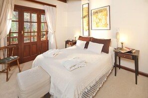 A neatly arranged bedroom with a large bed, a wooden chair, a small table, and a door with curtains. - La Mansión del Bosque (Mar de Las Pampas)