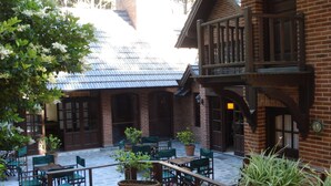 A courtyard with wooden tables and chairs, potted plants, and a brick building with a blue roof.
