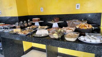Buffet com diversos alimentos e um bolo em um balcão preto e amarelo.