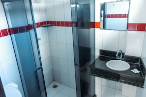 Une salle de bain avec une douche à parois de verre, un lavabo doté d’un plan de travail noir et des murs carrelés de rouge et de blanc.