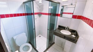 Un baño con ducha envuelta en vidrio, inodoro blanco y lavamanos con espejo.
