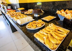 A buffet with various food items including bread, pastries, and a cake. - HOTEL PIRÂMIDE IGUATEMI (Salvador)