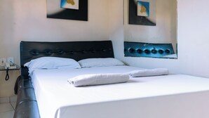 Una habitación de hotel con una cama, una mesita de noche, un teléfono y un espejo fijado a la pared.