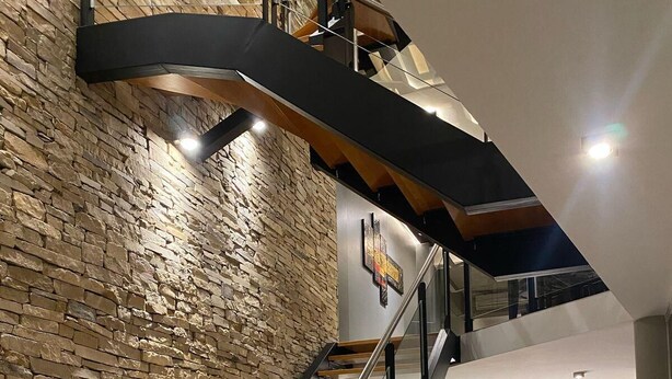 A modern interior with a wooden staircase, stone wall, and a reception desk. - Hotel Aires de Tandil (Tandil)