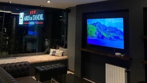 A modern hotel room with a large flat-screen TV, a comfortable sofa, and a glass wall with a sign for 'Aires de Tandal Hotel'. - Hotel Aires de Tandil (Tandil)
