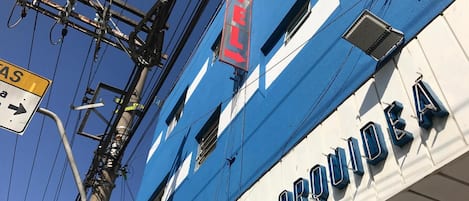 Um hotel com fachada azul e branca, uma placa indicando uma direção à direita e o nome 'HOTEL ORQUEA' exibido no edifício.