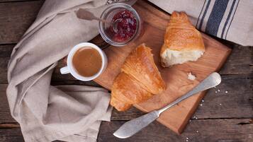A wooden table with a croissant, a jar of jam, and a cup of coffee.