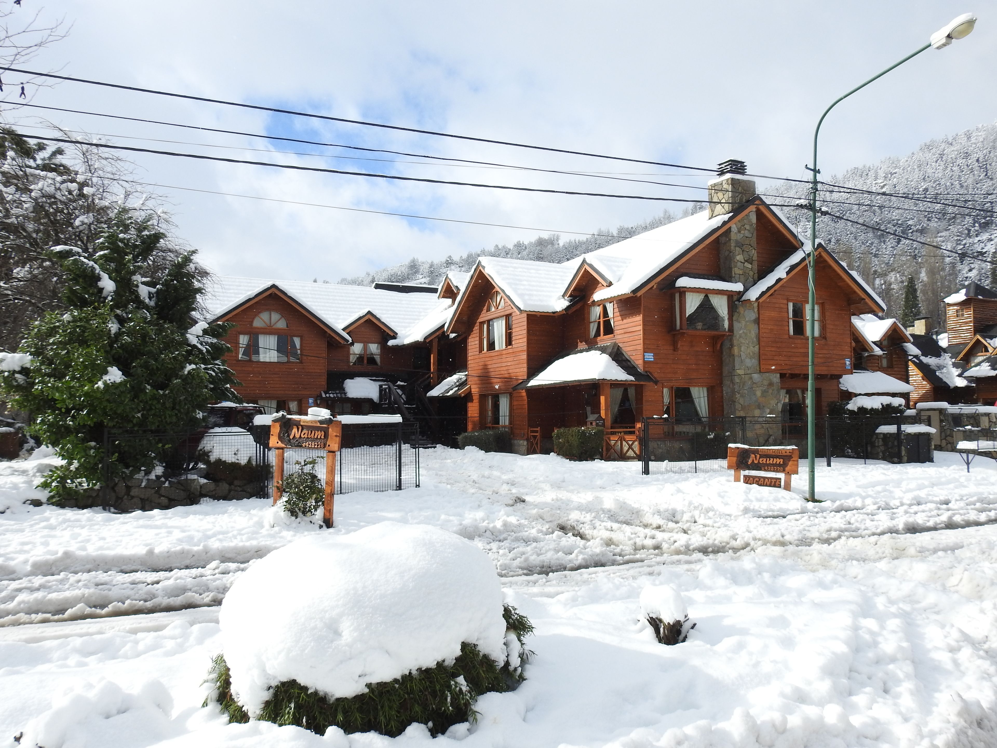 A snow-covered lodge with multiple wooden buildings, a stone chimney, and a signboard.