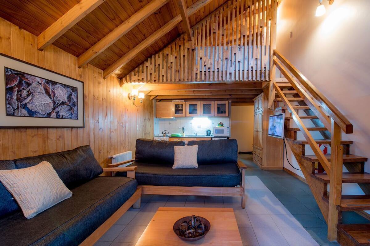 A cozy wooden interior with a sofa, a coffee table, and a staircase.