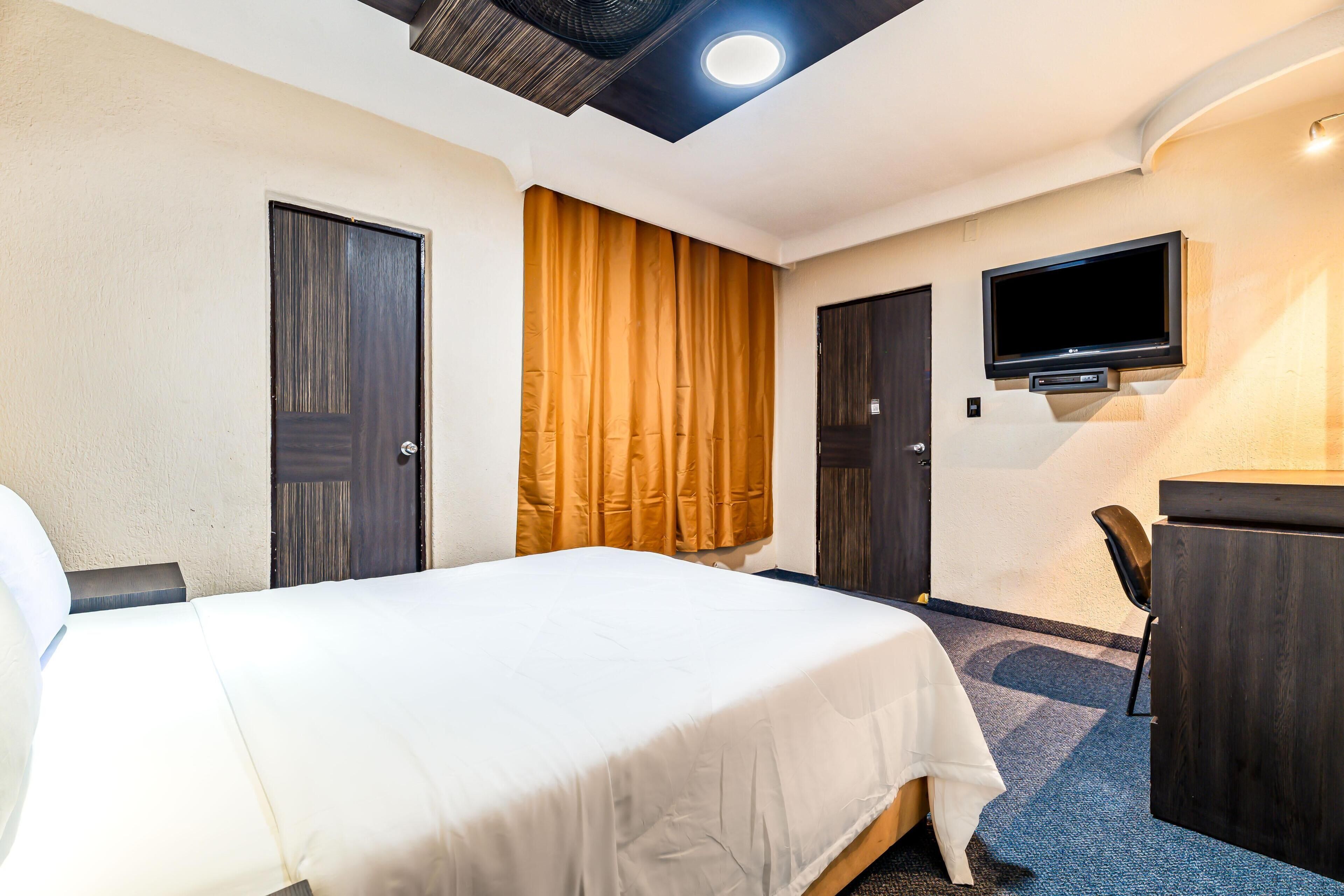 Una habitación de hotel con cama, escritorio, televisor y puerta.