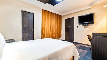 Una habitación de hotel con cama, escritorio, televisor y puerta.