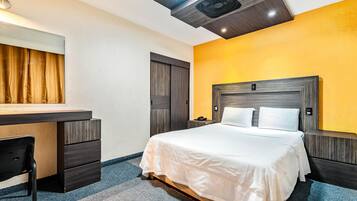 Una habitación de hotel con una cama, un escritorio, una silla, un espejo y un ventilador de techo.