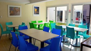 A dining area with tables and chairs, framed artwork on the walls, and a door with a sign. - Jaque Mate Hostel (Mendoza)